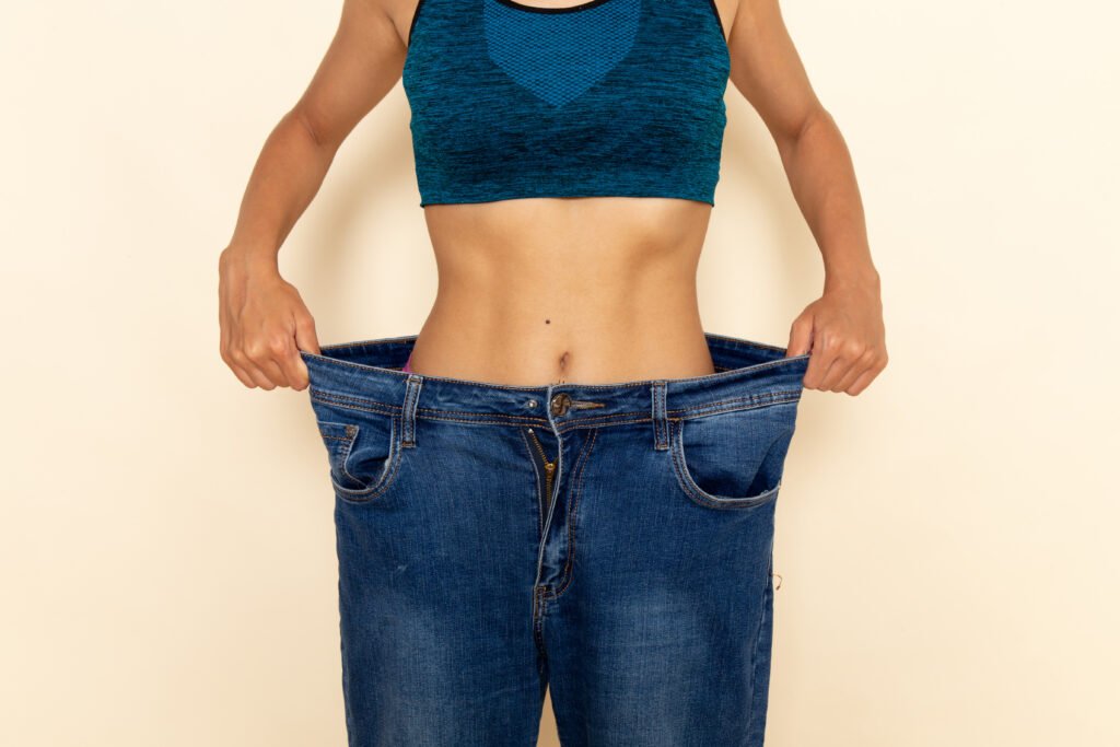 Liposuccion ventre 46 front view young female with fit body blue shirt jeans light white wall