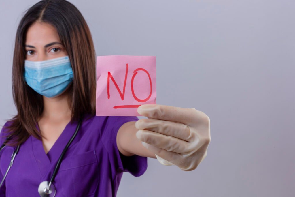 Quels sont les risques et effets secondaires d’une liposuccion ? 2 young woman nurse wearing medical uniform protective mask gloves with stethoscope showing reminder paper with word no looking confident